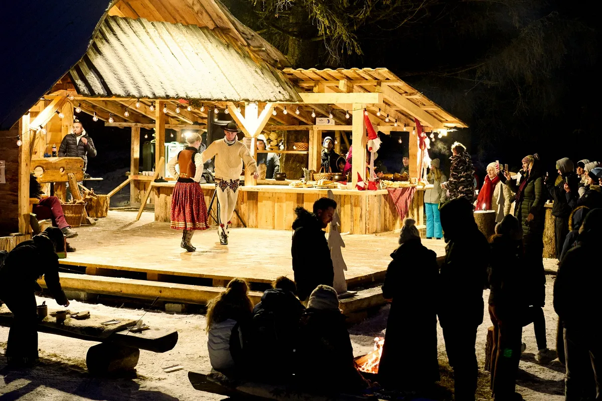 Biesiada góralska pod drewnianą wiatą nocą - goście przy scenie i ognisku